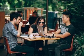 A group of young adults at a coffee shop, on laptops