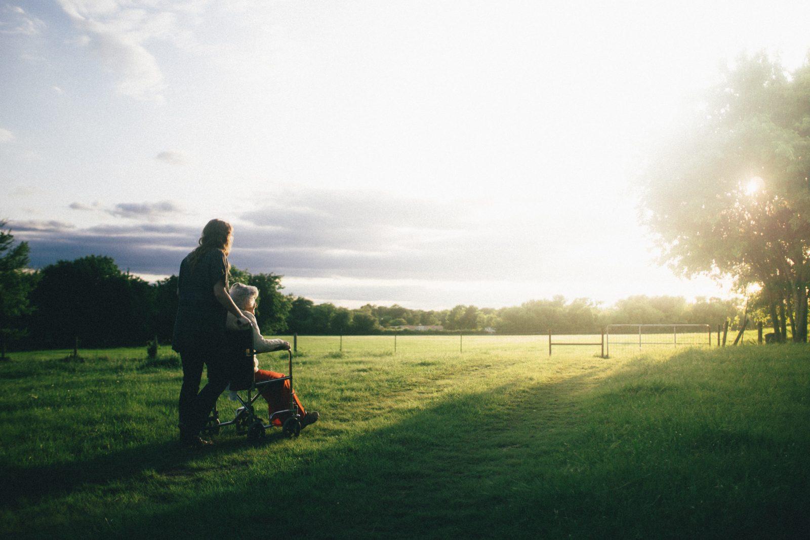 woman pushing person across lawn in wheelchair